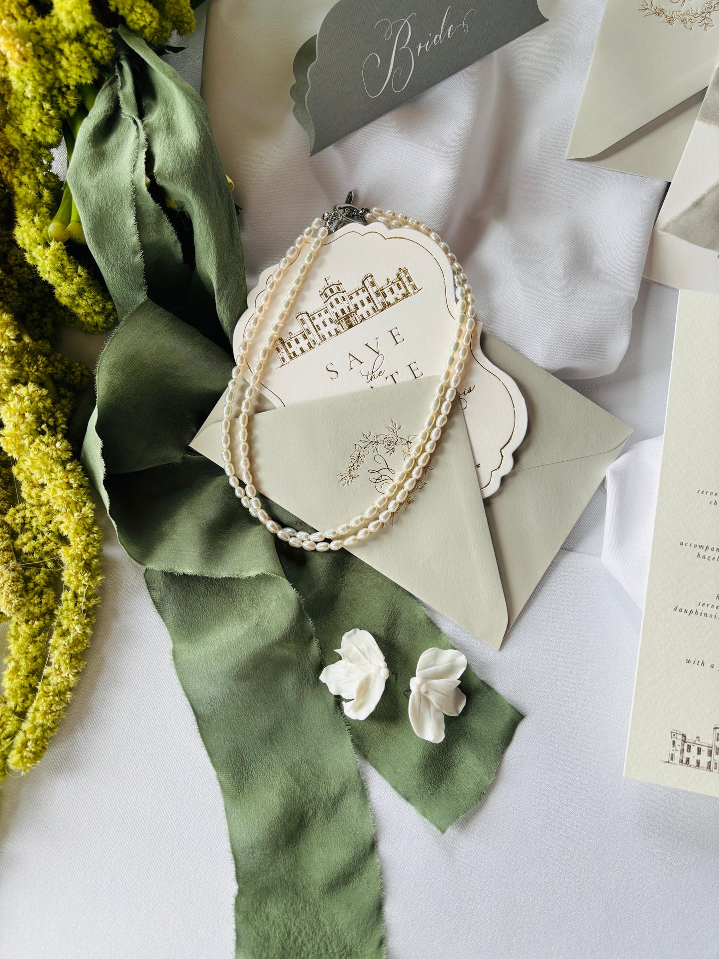 Wedding invitation with green ribbon and pearl details on a white surface
