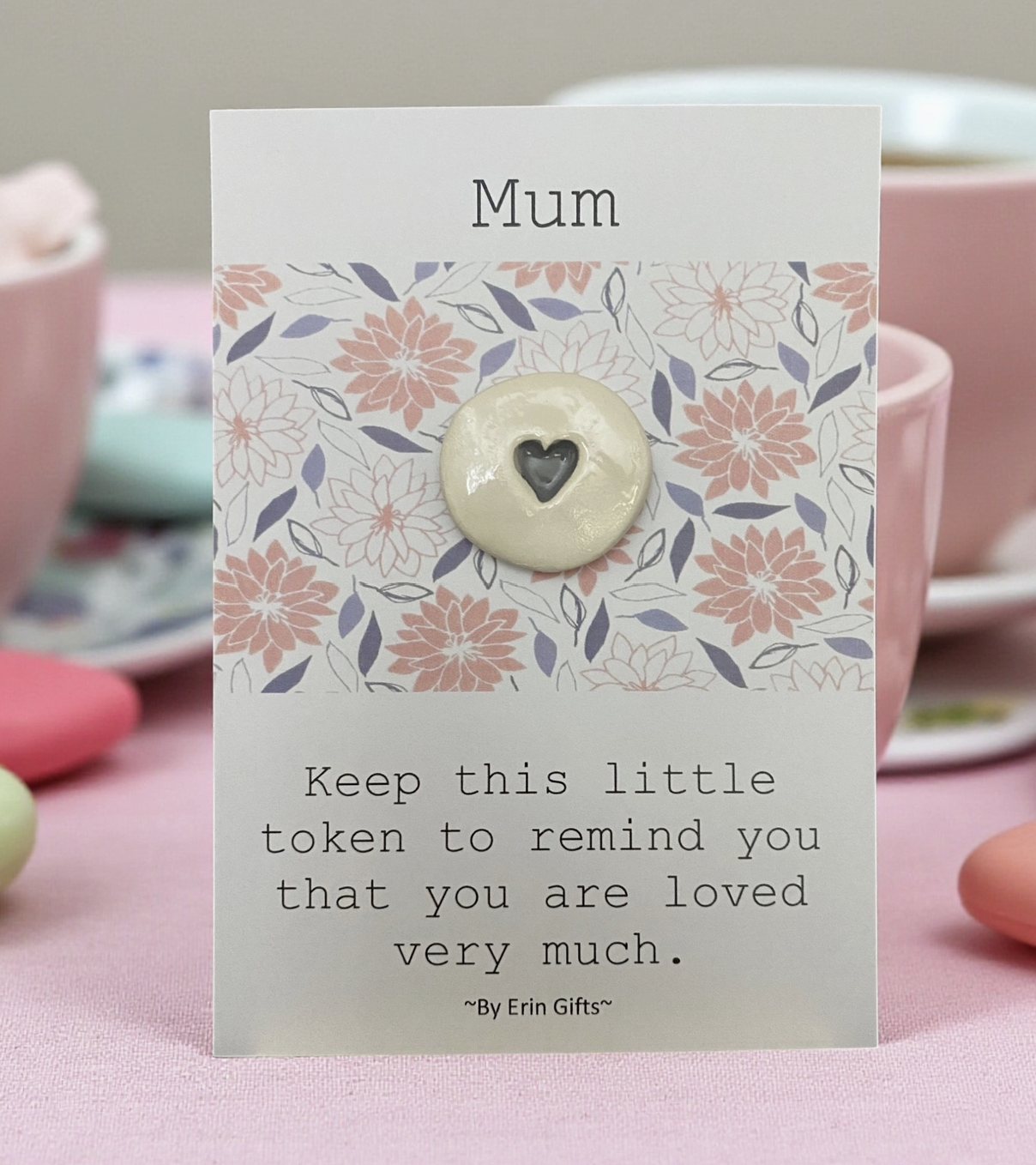 Card with floral design and button featuring a heart, on a table with tea cups.