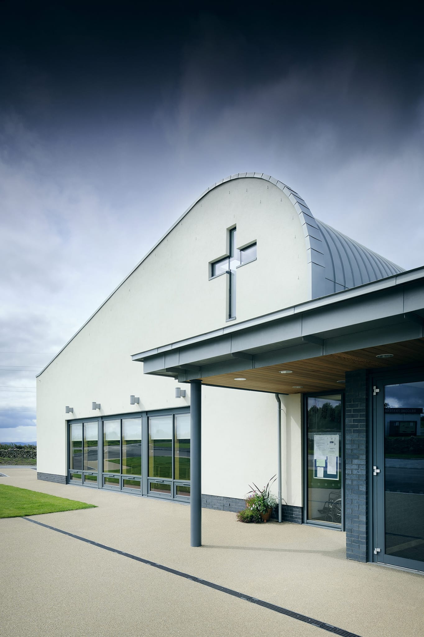 Modern church building with a cross on the facade against a cloudy sky.