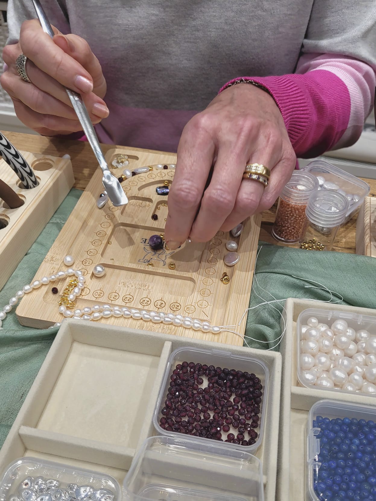 Person working on a jewelry project with beads and tools on a table.