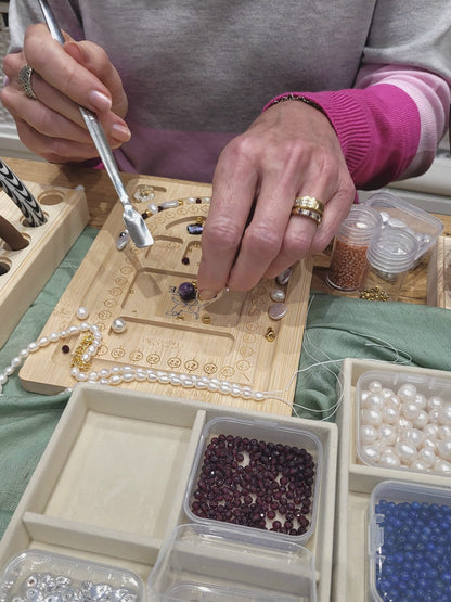 Person working on a jewelry project with beads and tools on a table.