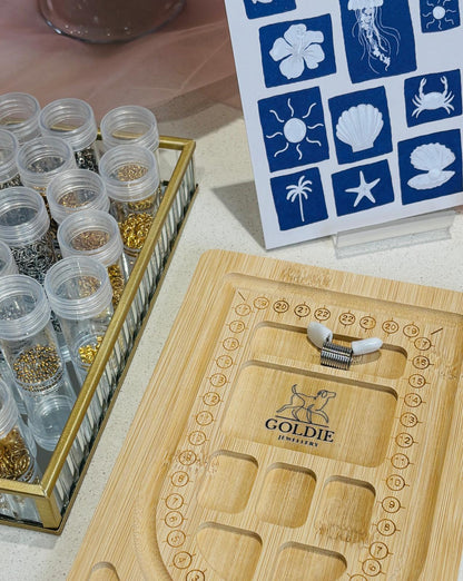 Goldie jewelry display with wooden tray and small containers on a table.