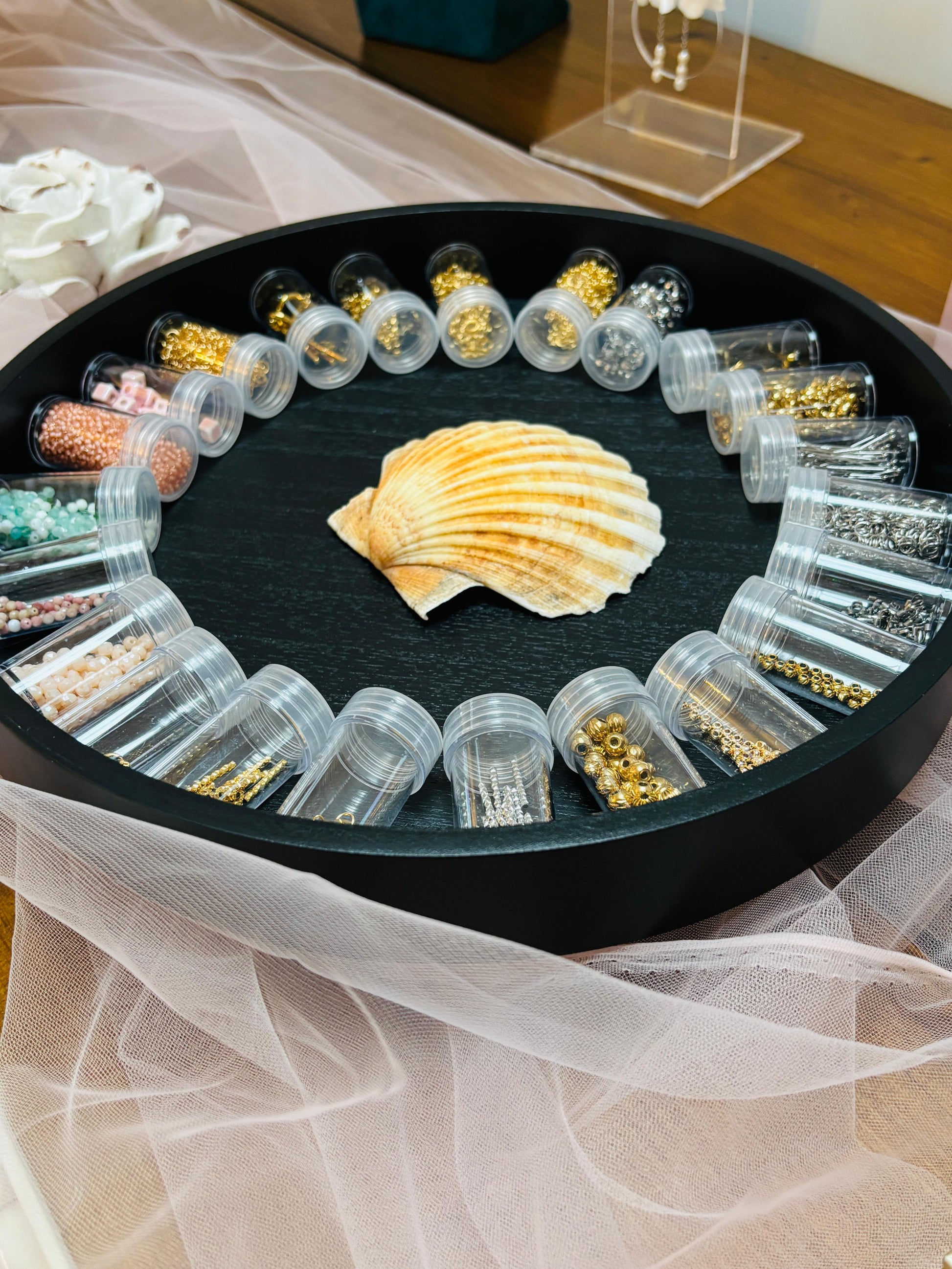 Round black tray with small containers holding jewelry components on a white fabric background.