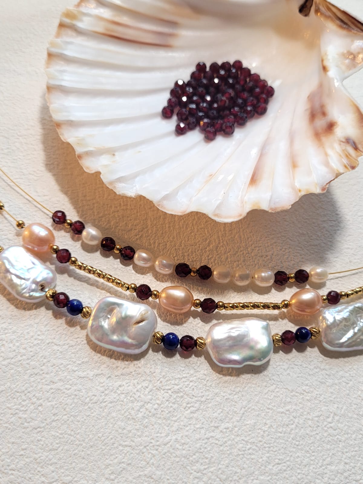 Pearl and gemstone necklace on a shell with a textured beige background