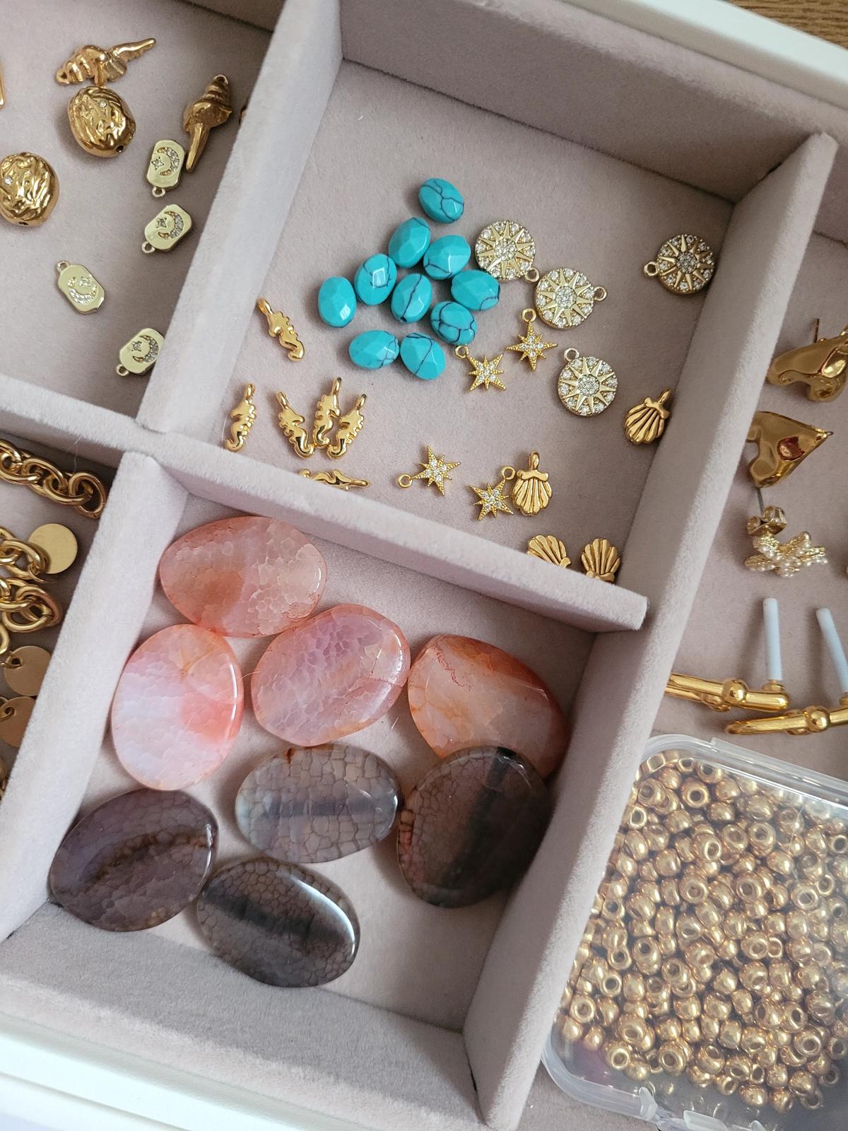 Jewelry box with gold and silver jewelry, turquoise stones, pink stones, and gold beads.