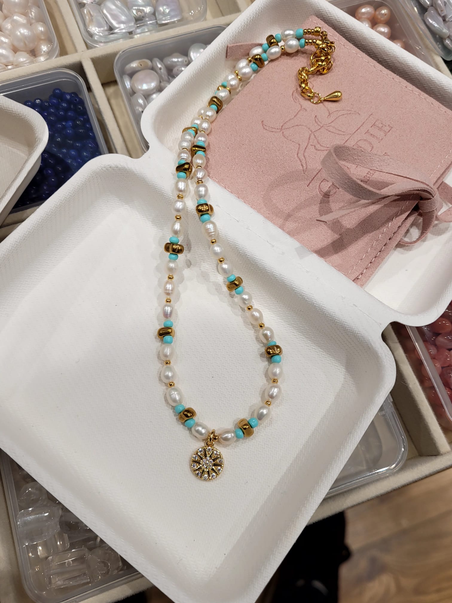 Necklace with pearls and turquoise beads on a white tray with jewelry-making materials.